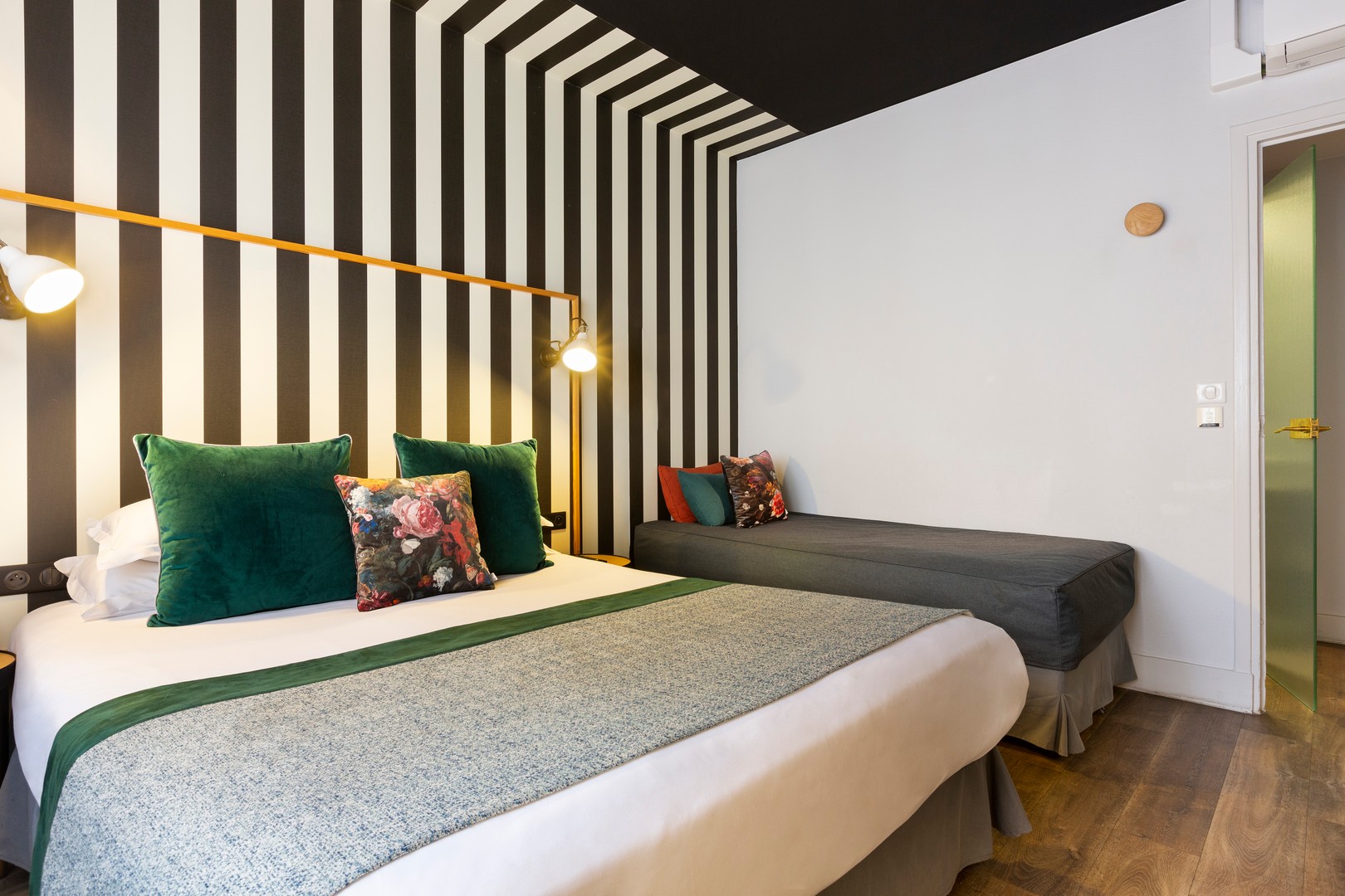 Double room for triple occupancy: double bed with green and floral cushions, single bed further back, black and white striped wall and ceiling